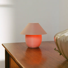 Small table lamp with a pinkish-red shade on a wooden surface.