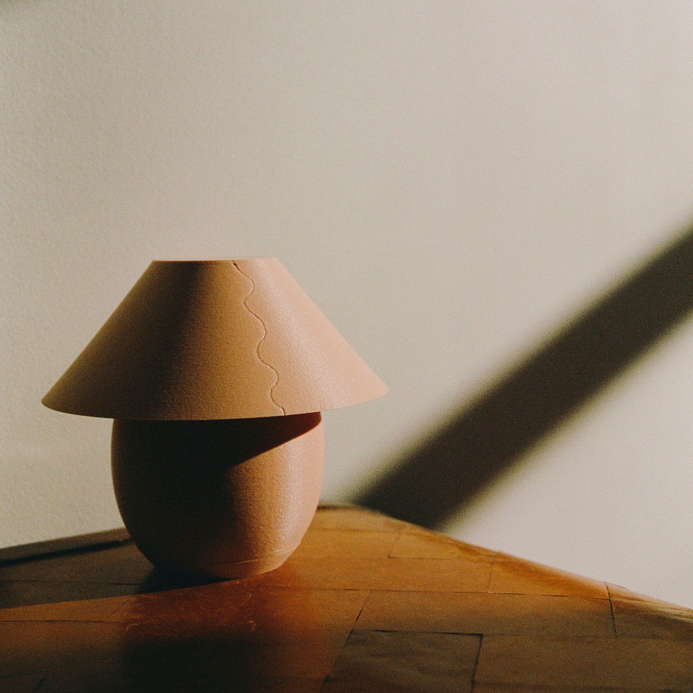 Pink ceramic lamp on a wooden surface with a soft shadow on a light background