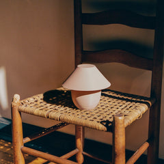 White lamp on a woven stool against a textured wall
