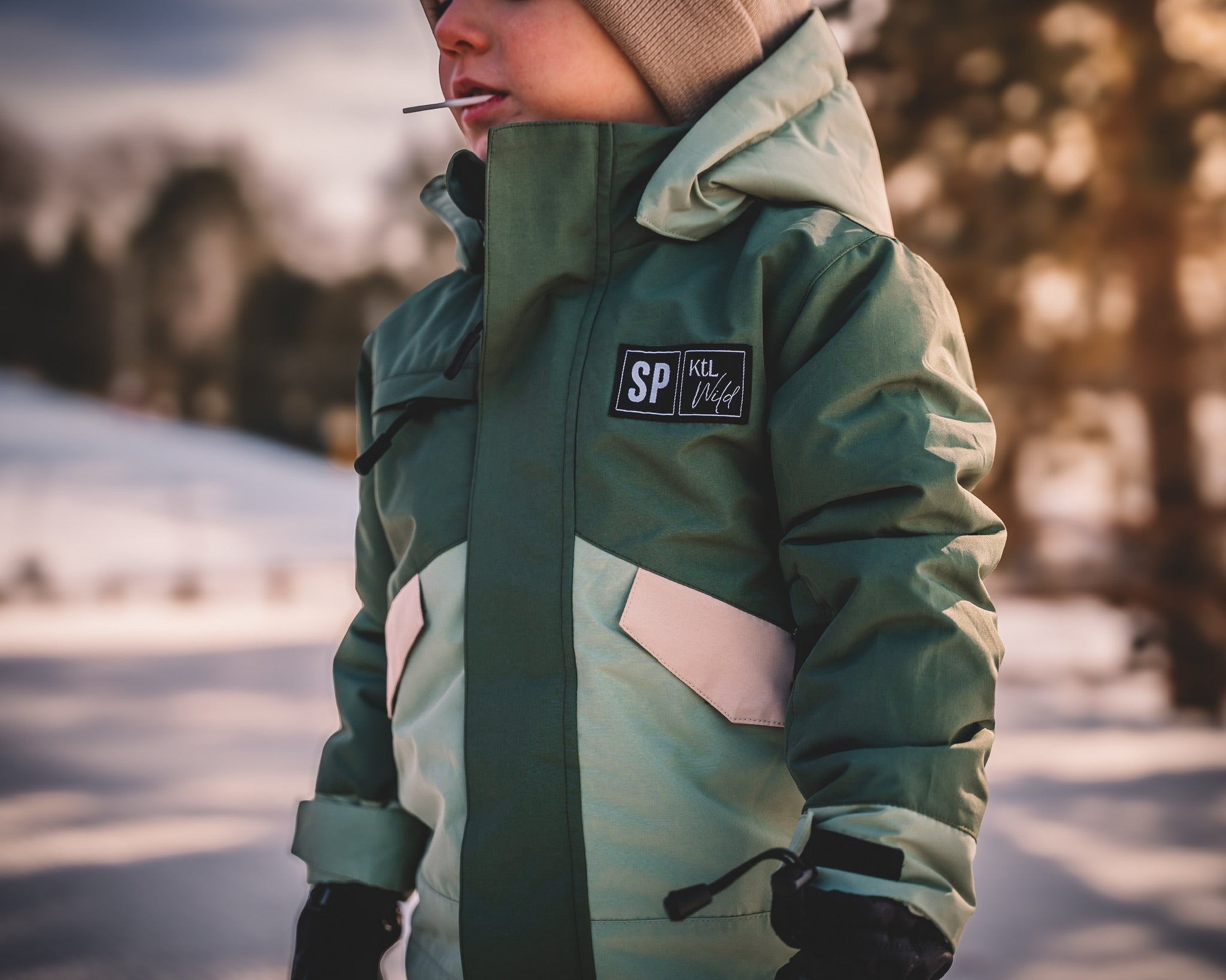 Person wearing a green winter jacket with a brand logo in a snowy landscape