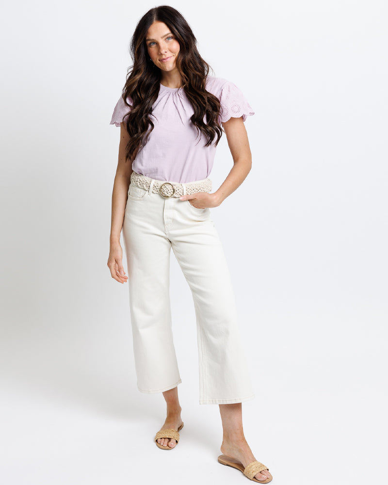 Woman wearing a light purple blouse and white pants on a white background