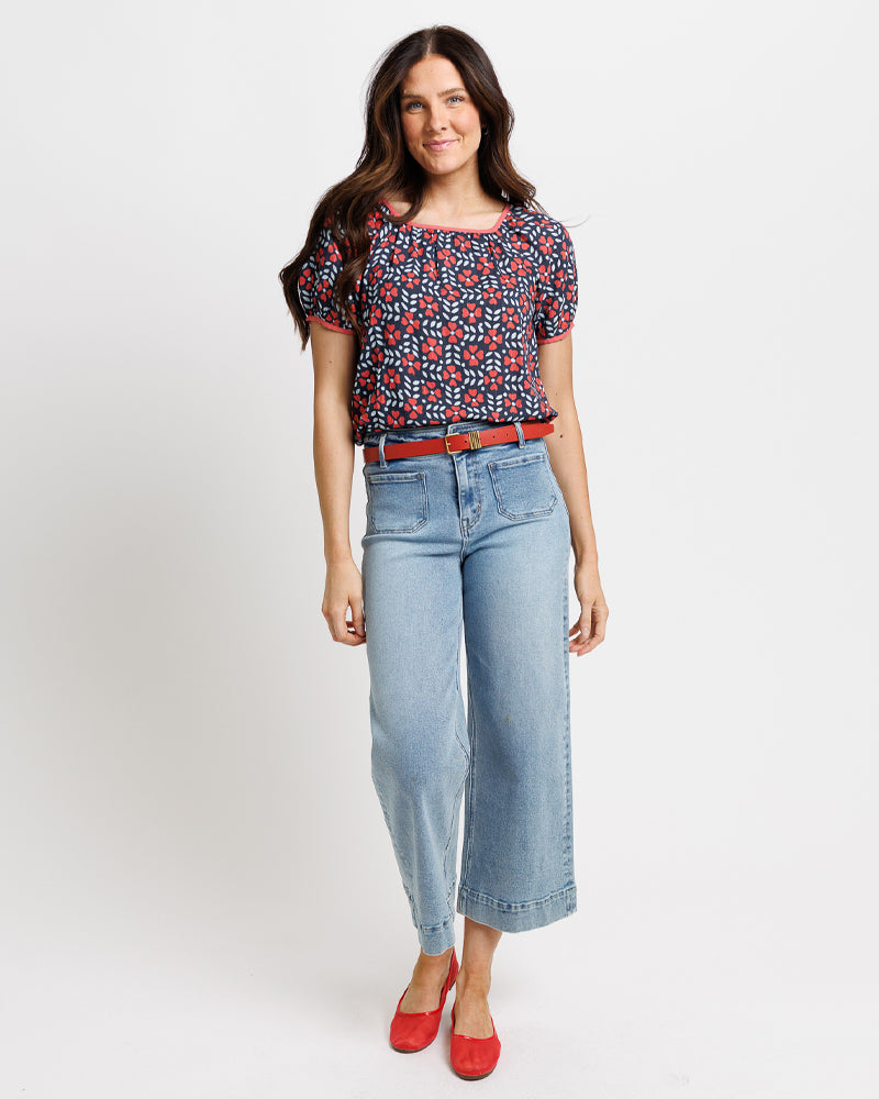 Woman wearing a floral blouse, jeans, and red shoes on a white background