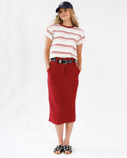 Woman wearing a red skirt, striped shirt, and cap on a white background