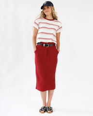 Woman wearing a red skirt, striped shirt, and cap on a white background