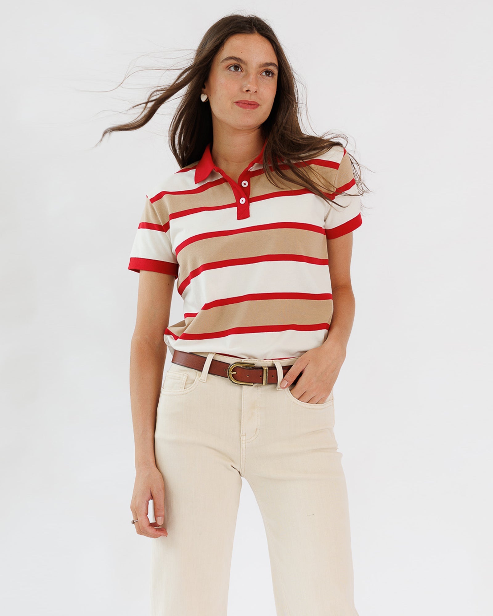Woman wearing a red and beige striped polo shirt with white pants on a light gray background
