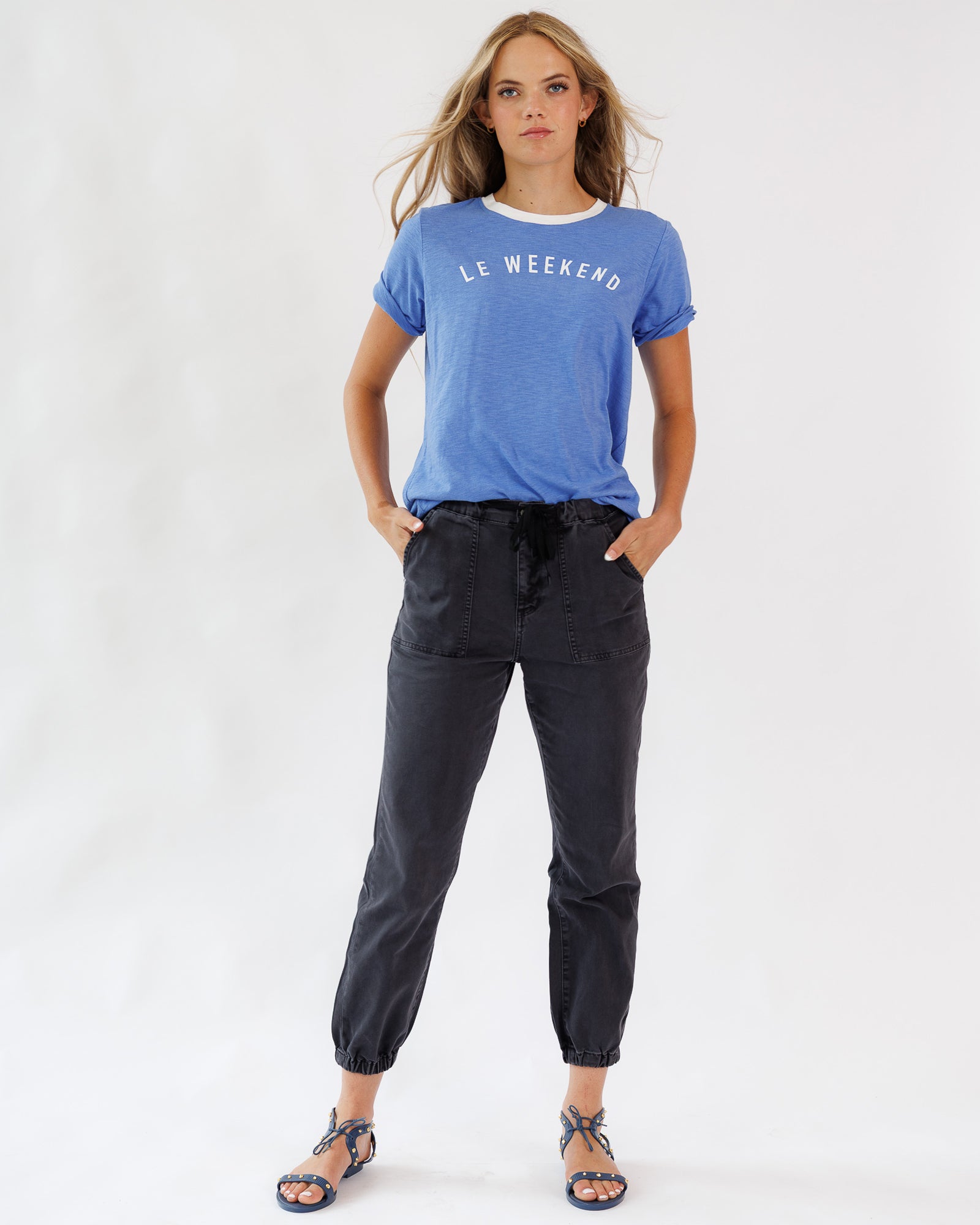 Woman wearing a blue t-shirt with 'Le Week-end' text and black pants on a white background