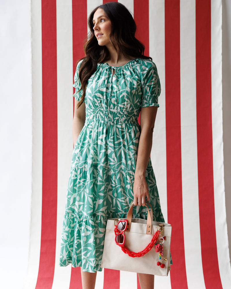 Woman in a green dress holding a beige handbag with red accents against a red and white striped background
