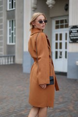Woman wearing a brown coat and sunglasses walking on a street.