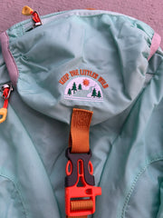 Close-up of a teal bag with a embroidered patch and orange strap.