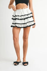 Person wearing a white skirt with black ruffles on a plain background