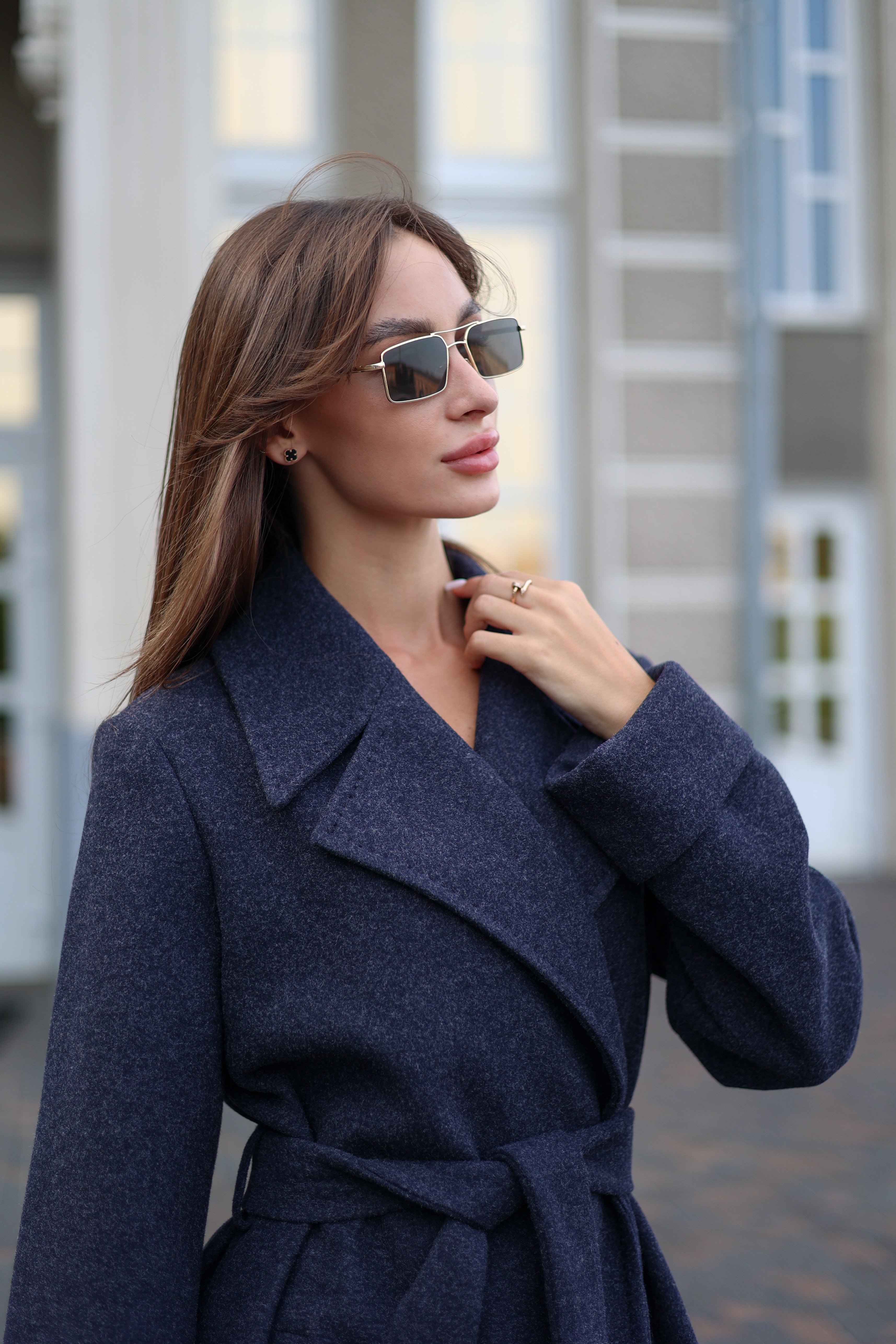 Woman wearing a dark blue coat and sunglasses outdoors.