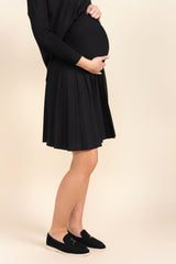 Pregnant person wearing a black dress and shoes on a beige background