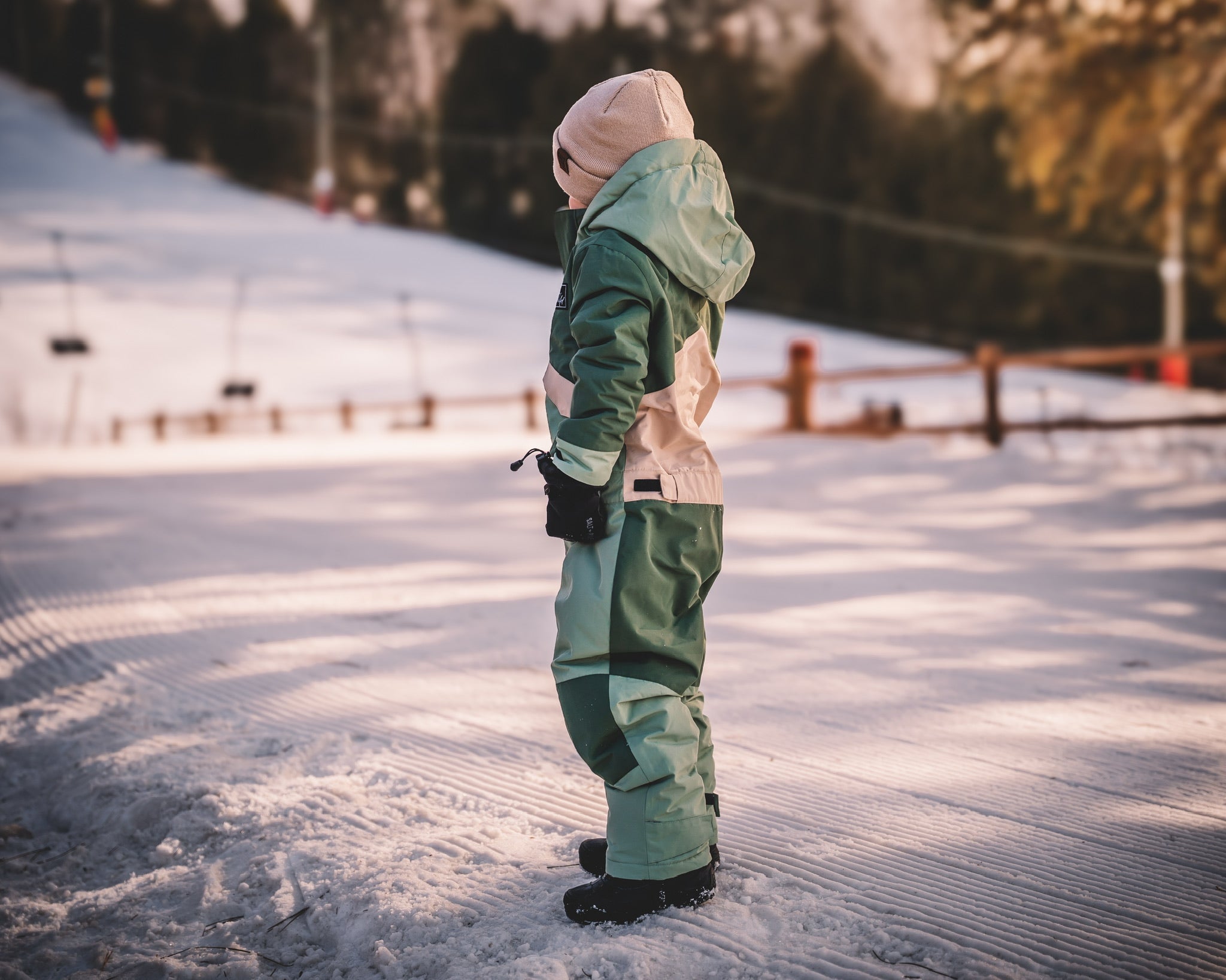 Person in green snowsuit standing on a snowy landscape with trees in the background