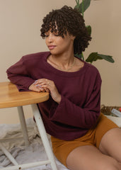 Woman wearing a maroon sweater and mustard shorts sitting at a table.
