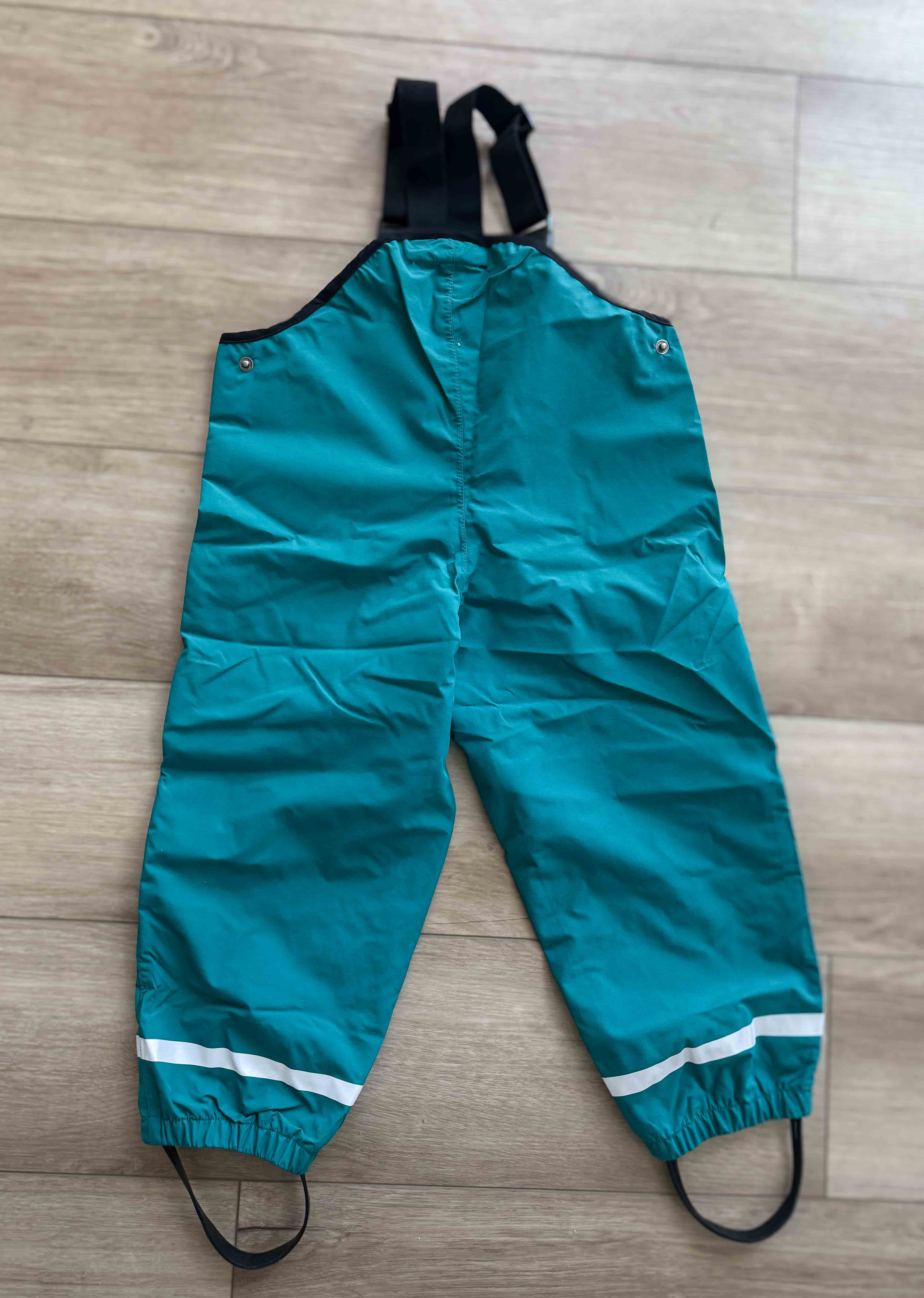Teal rain pants with suspenders on a wooden floor