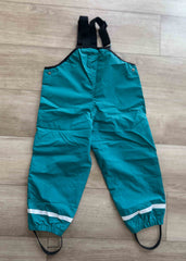 Teal rain pants with suspenders on a wooden floor