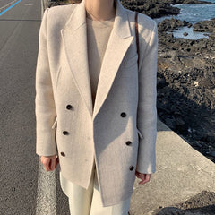 Person wearing a beige double-breasted coat with black buttons by a rocky coastal area.