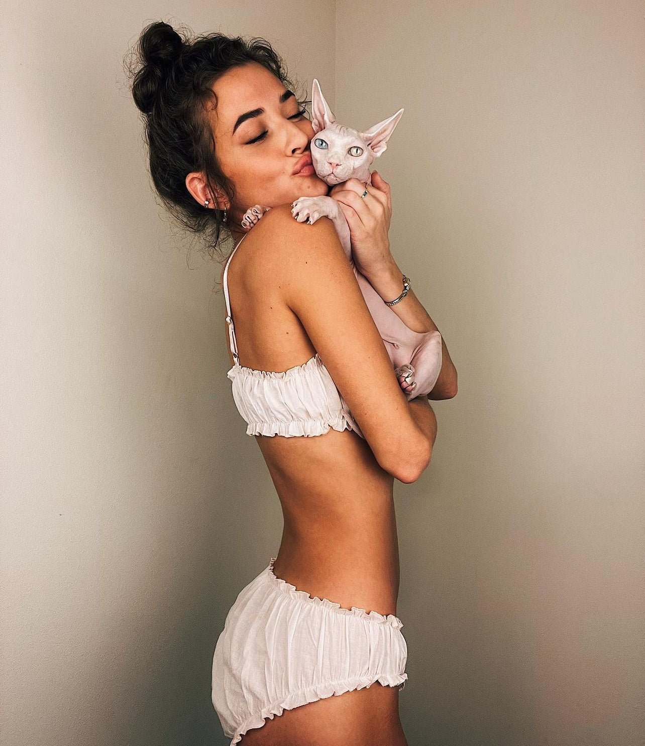 Woman in white lingerie holding a white cat against a beige background