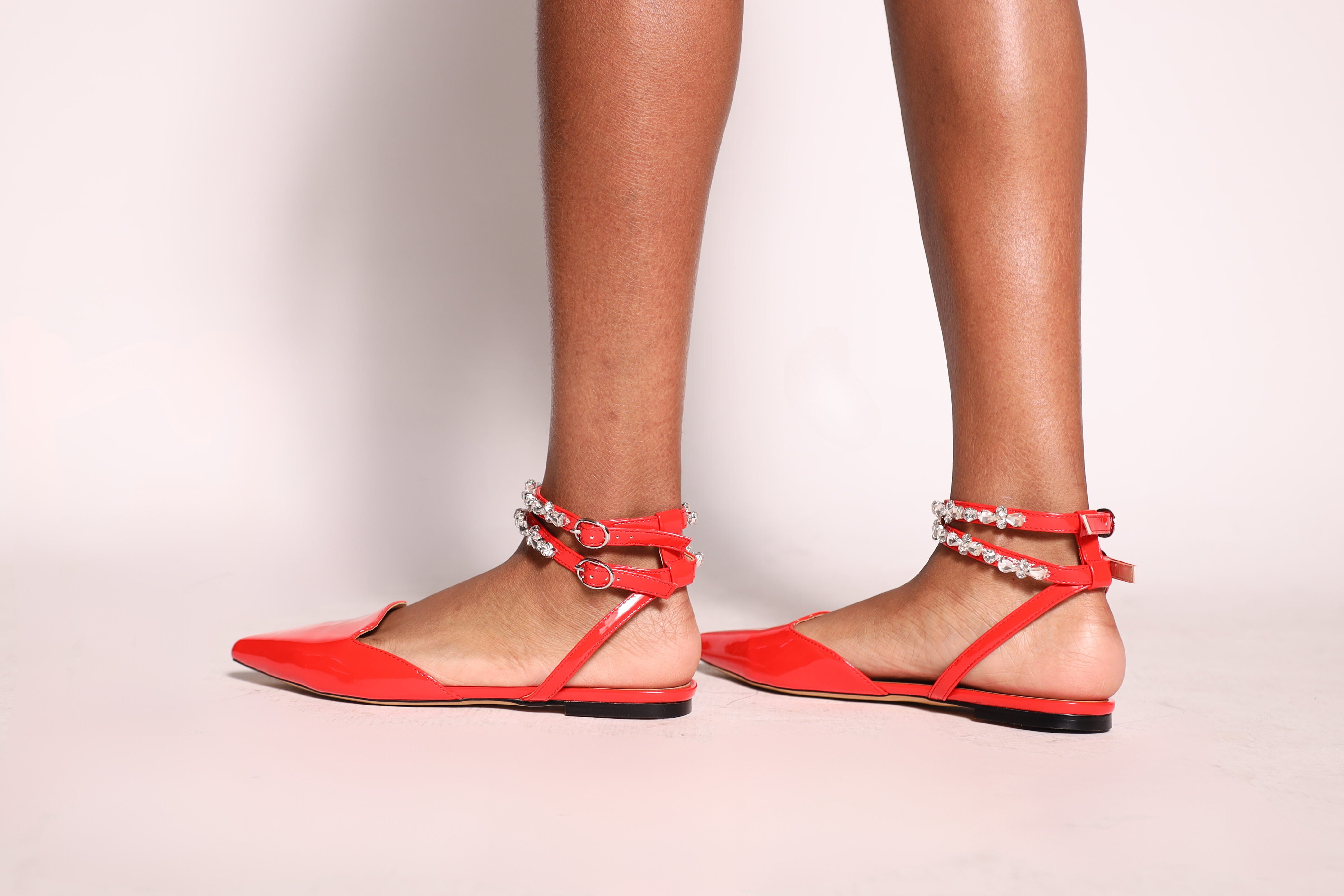 Red flat sandals with ankle straps worn by a person on a light pink background