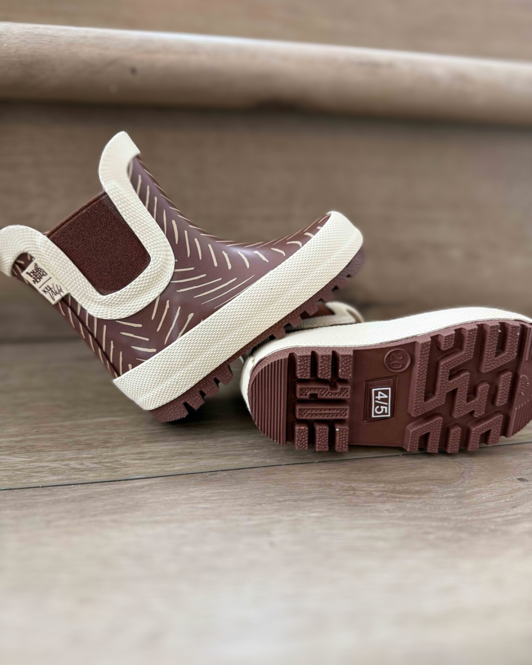 Pair of brown rain boots with white soles on a wooden floor.