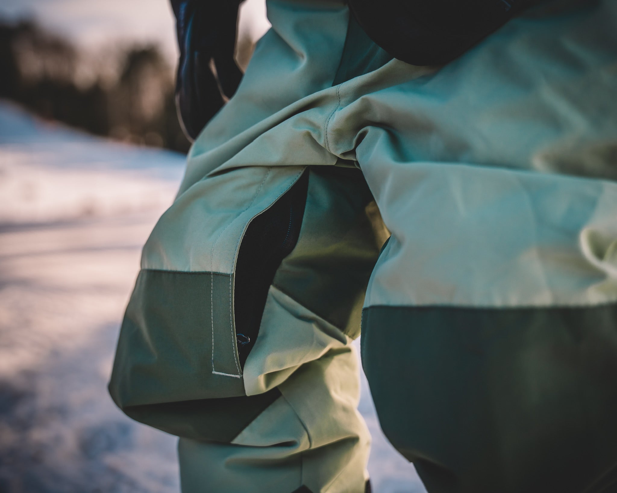 Close-up of a person wearing a light green jacket with a blurred snowy landscape in the background