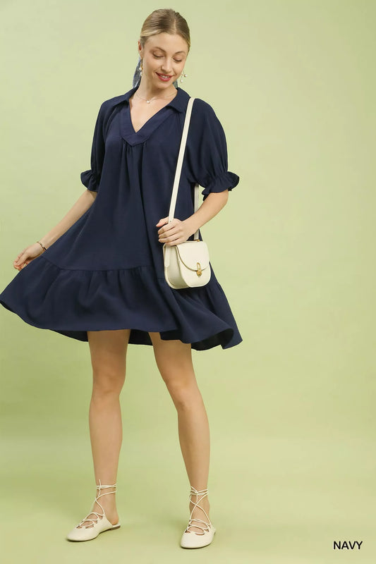 Woman wearing a navy dress with a white handbag on a light green background
