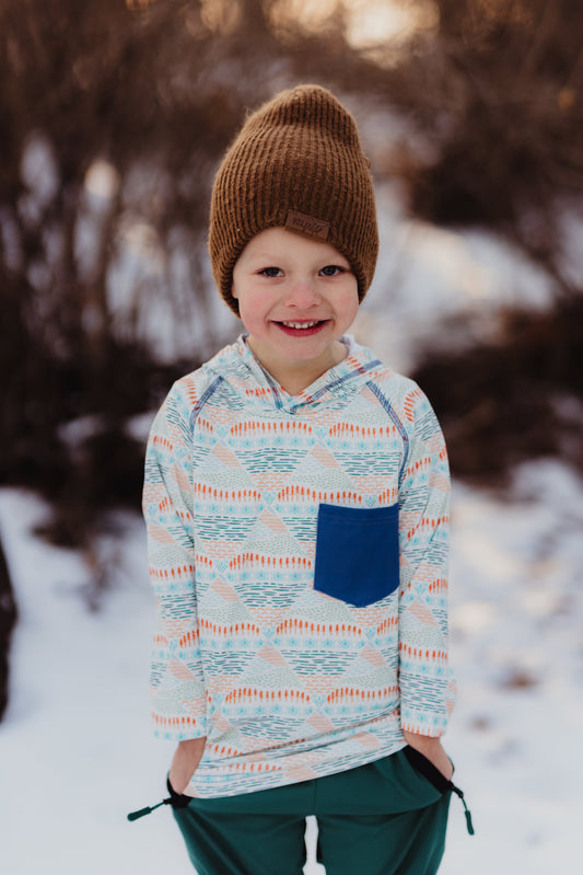 Child wearing a patterned hoodie and brown knit hat in a snowy outdoor setting