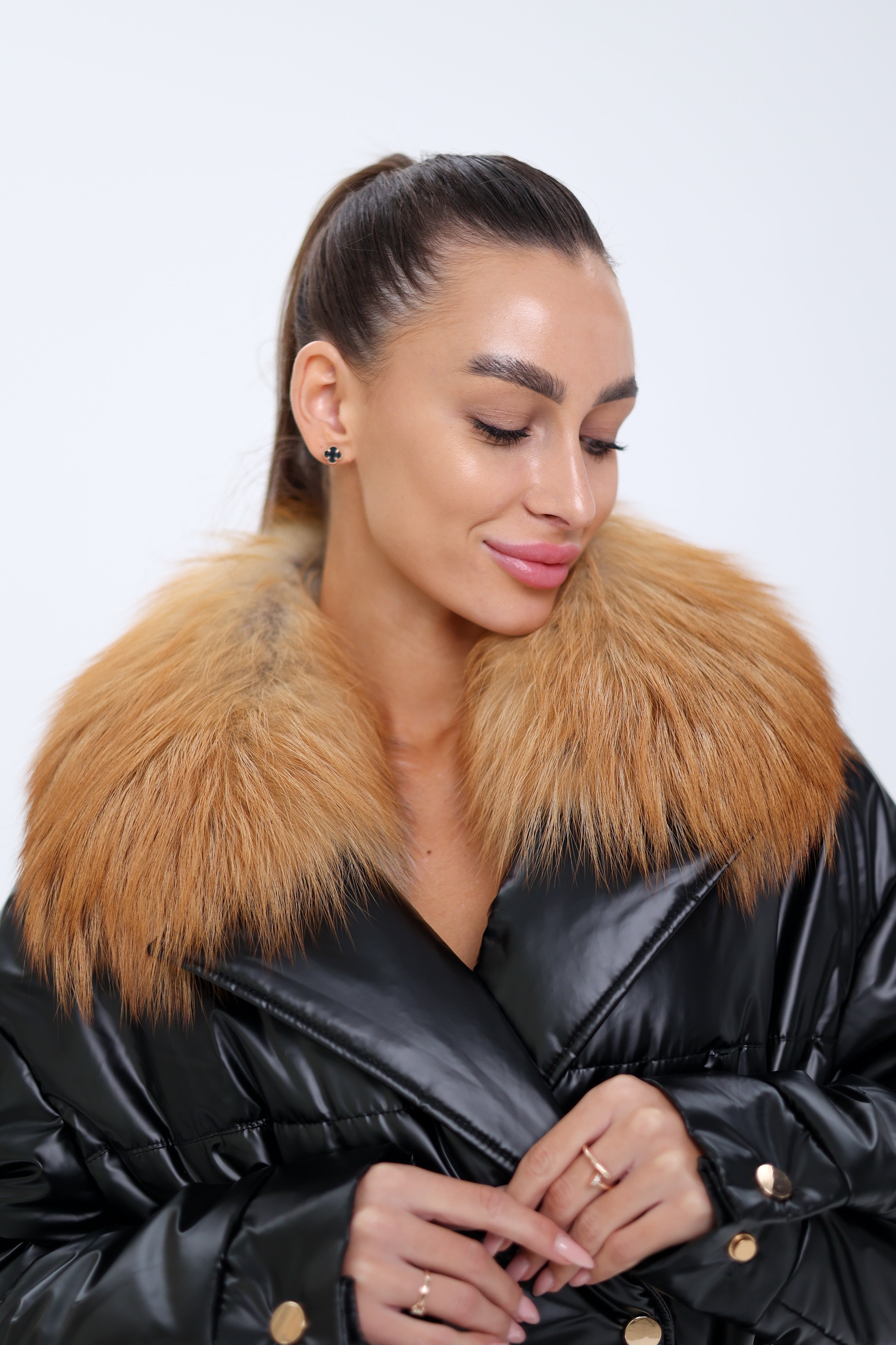 Woman wearing a black puffer jacket with a fur collar on a white background