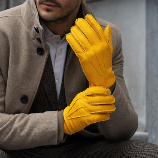 Man wearing a brown coat and yellow gloves against a neutral background