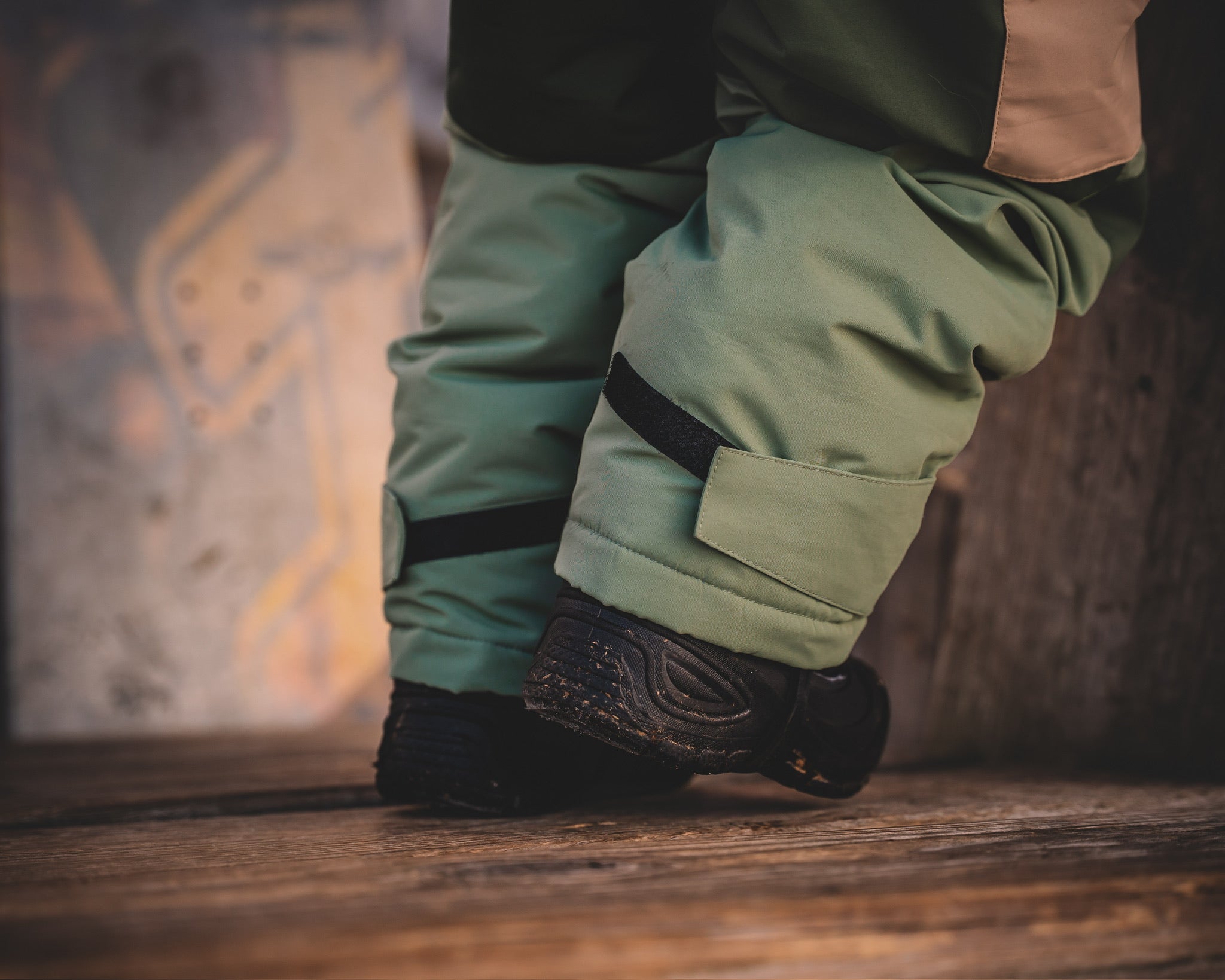 Close-up of green pants and black shoes on a wooden floor.