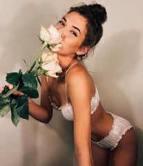 Woman in white lingerie holding a bouquet of roses against a plain background