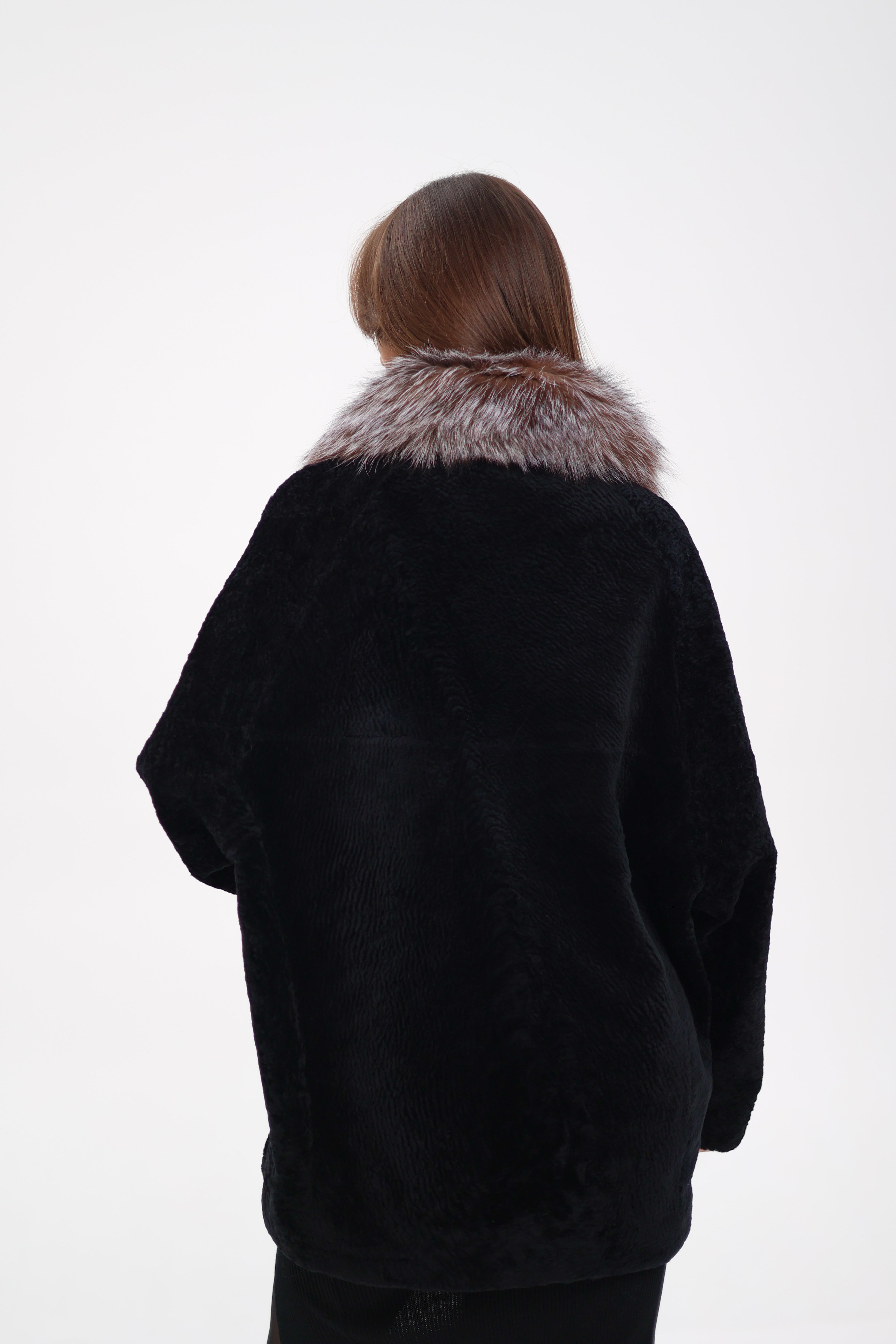 Person wearing a black coat with fur collar on a white background