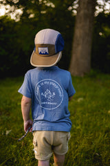 Child wearing a blue shirt and cap in a grassy outdoor setting