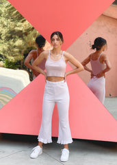 Woman in a pink tank top and white pants standing in front of a colorful geometric background.