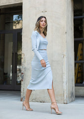 Woman in a light blue outfit standing against a concrete wall.