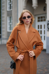 Woman wearing a brown coat and sunglasses outdoors.