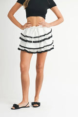 Person wearing a white skirt with black trim and a black top on a light gray background