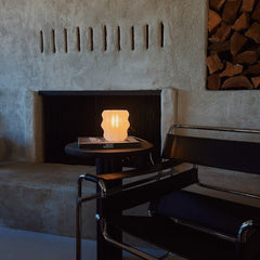 Modern chair in front of a stone fireplace with a small table and lamp.