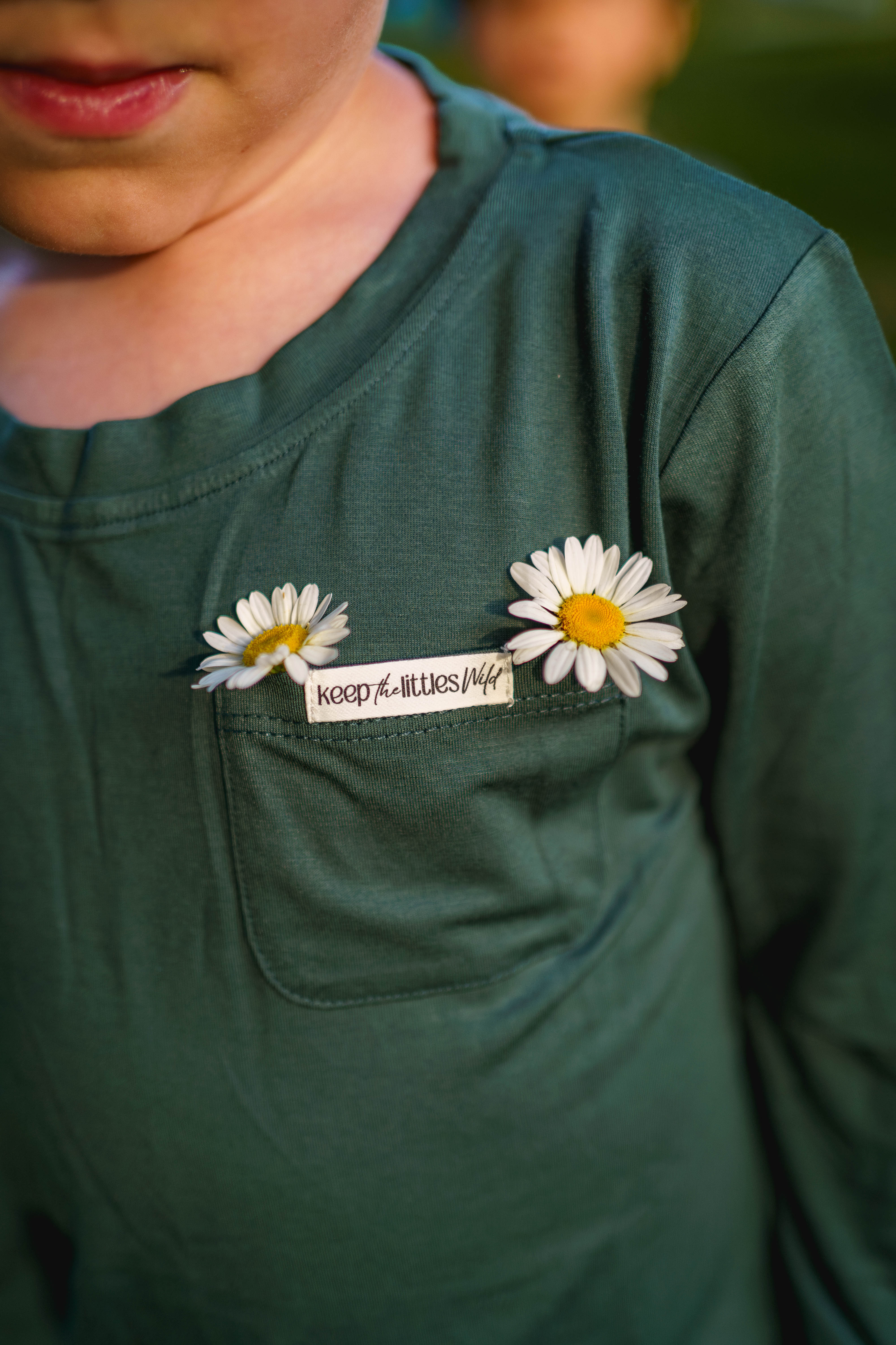 Green shirt with daisy pins and a brand logo on a blurred background