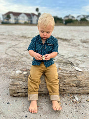 Child sitting on a log at the beach holding a shell