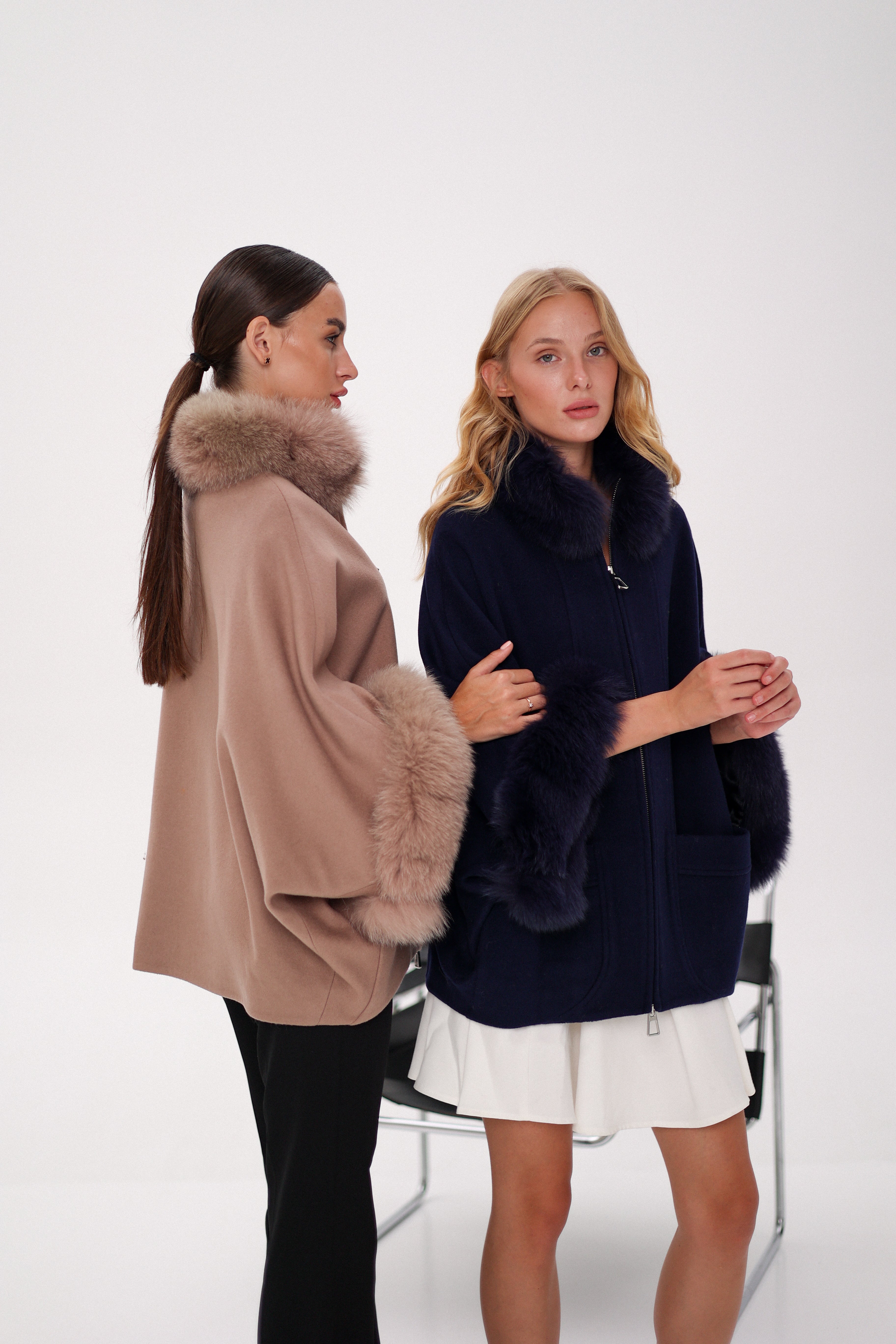 Two women wearing fur-lined coats on a white background