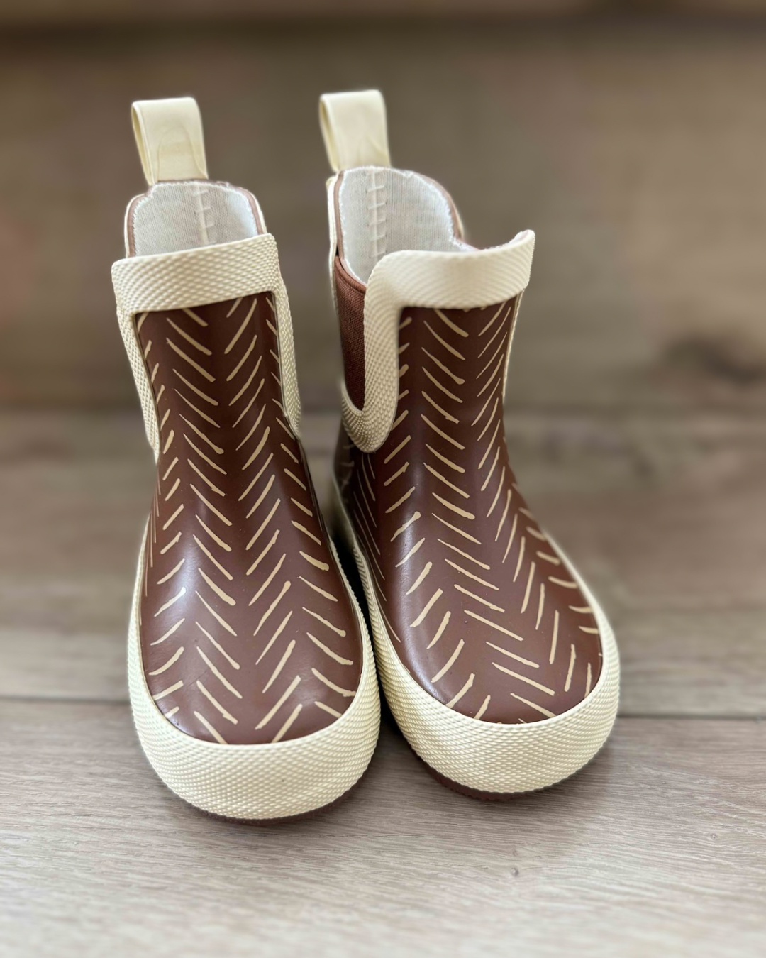 Pair of brown rain boots with white patterns on a wooden surface