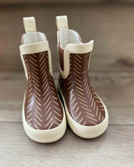 Pair of brown rain boots with white patterns on a wooden surface