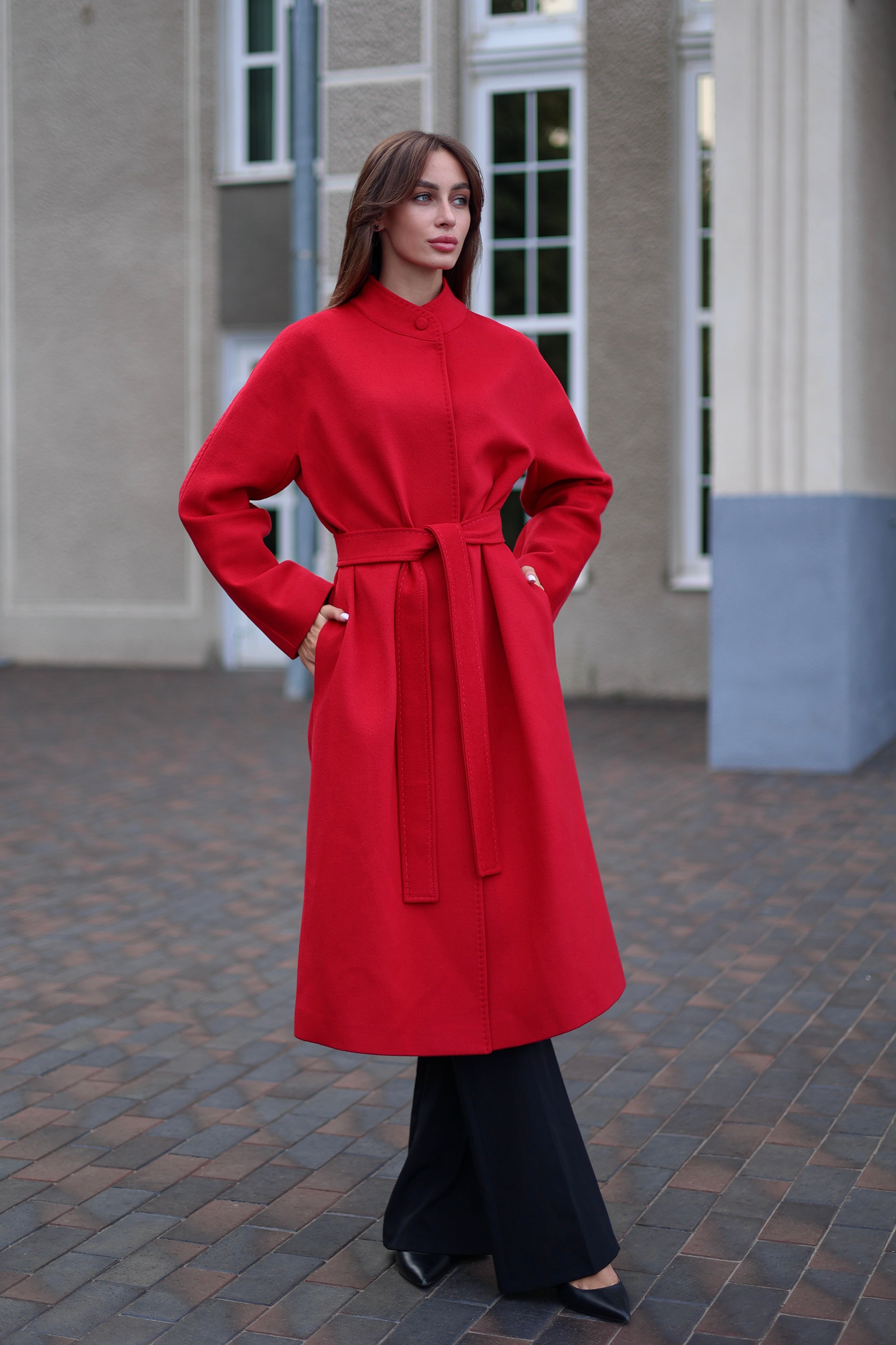 Woman wearing a red coat standing on a cobblestone street.