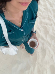 Person in teal pajamas holding a cup of coffee on a sandy surface