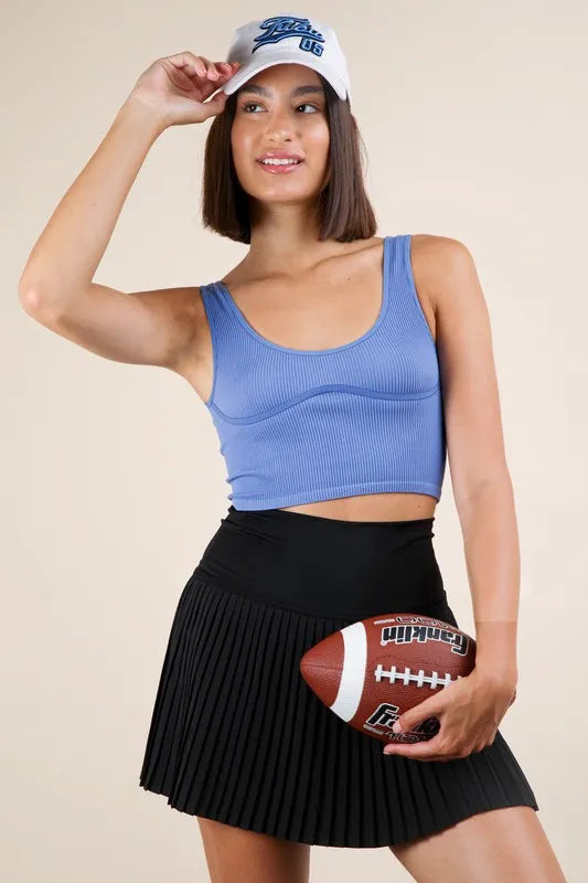 Woman wearing a blue sports bra and black skirt, holding a football, with a beige background
