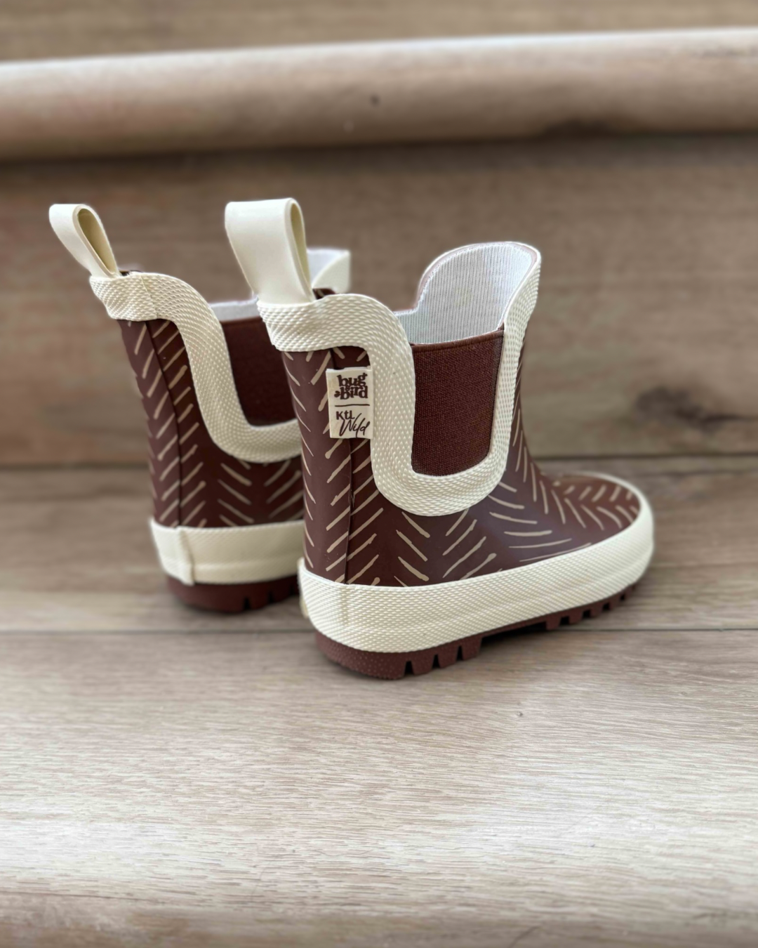 Pair of brown and white children's rain boots on a wooden surface