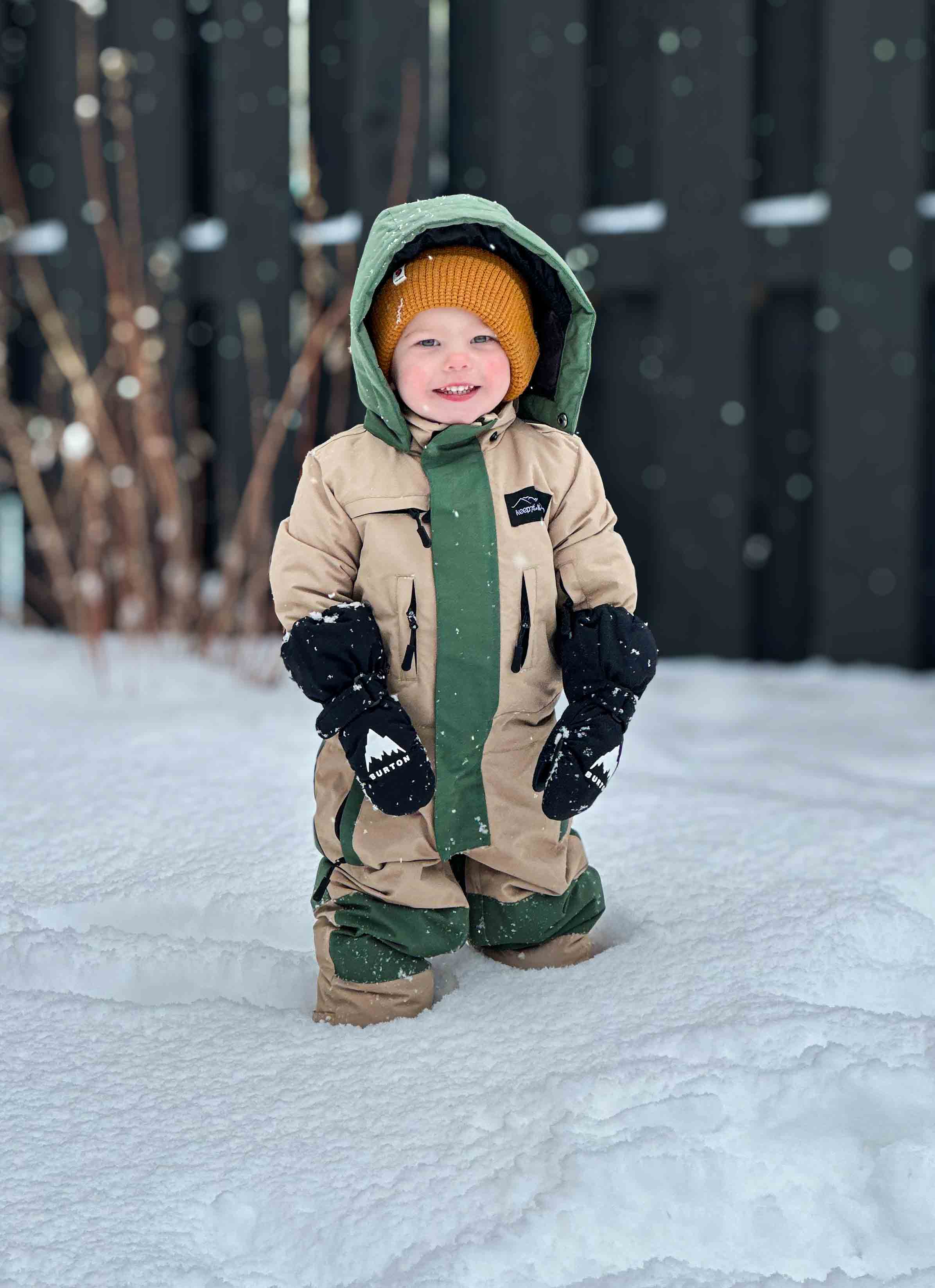 Child in a snowsuit standing on a snowy ground with a dark background