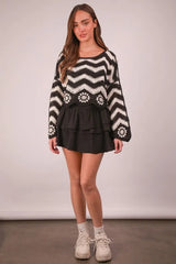 Woman wearing a black and white patterned sweater with a black skirt on a plain background