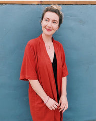 Woman wearing a red cardigan over a black top against a blue wall